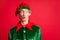 Photo of astonished elf guy look into empty space wear green costume pointy hat isolated over red color background