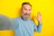 Photo of attractive friendly retired guy wear blue sweater tacking selfie waving arm palm isolated yellow color