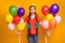 Photo of attractive funny lady hold many air balloons hands birthday party best friend blow noisemaker wear paper cone