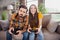 Photo of attractive funny young lovers dressed casual clothes sitting sofa smiling holding playstation joystick indoors