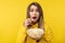 Photo of attractive lady holds plate of popcorn, eats it with shocked face. Wears casual yellow hoody, isolated yellow