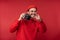 Photo of attractive man with beard in glasses and red clothing. Happy man holds camera and looks nice,  over red