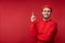 Photo of attractive man with beard in glasses and red clothing. Nice and cute male points up,  over red