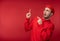 Photo of attractive man with beard in glasses and red clothing. Shocked and puzzled male points up,  over red