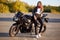 Photo of attractive woman has real adventure outdoor, stands near motorbike, dressed in bikers outfit, enjoys sunny day and calm a