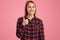 Photo of attractive woman with toothy smile, dressed in checkered shirt, keeps thumb raised, gives approval to something, models