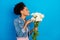 Photo of attractive young happy afro american woman hold hands flowers smell isolated on blue color background