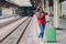 Photo of attractive young woman waits train at railway station, dressed in knitted sweater and jeans, stands near green bag, looks