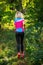 Photo from back of blonde athlete woman running through park among trees on summer.