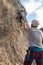 Photo from the back of the climbing belayer as the girl climbs a stone wall outdoors