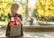 Photo from the back of young blonde dreamy woman with bouquet of flowers in grey backpack in a spring summer park