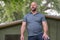 Photo of a bald man with beard posing outdoors with a blurry house in the background