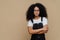 Photo of beautiful dark skinned teenage girl poses with arms crossed, wears spectacles, white t shirt and black sarafan, stands