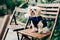 Photo of beautiful fluffy dog in festive clothes with bow tie, sits on wooden chair, waits for wedding ceremony outdoor. Animals