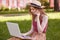 Photo of beautiful foxy haired woman sitting on green grass with laptop and phone in the hands, talking on phone, has important