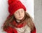 A photo of a beautiful little girl in a knitted red cap and big cosy scarf sleeping on a white bed and enjoying sweet win