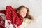 A photo of a beautiful little girl in a knitted red cap and big cosy scarf sleeping on a white bed and enjoying sweet win