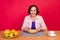 Photo of beautiful nice retired lady sit table eat lunch meal wear pink jacket isolated red color background