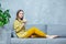 Photo of a beautiful young woman sitting with her legs on a sofa and holding in a hand a coconut with a straw. Concept