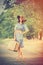 photo of beautiful young woman with suitcase standing on the road on the wonderful trees background