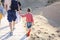 Photo from behind of happy family walking on wooden path on sunny sand beach