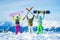 Photo from behind of three athletes with arms raised with snowboards and skis on day .