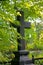 The photo of the black stone of the Christian cross on a background of sunlit abundant forest-Park greenery of trees, shrubs and