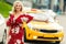 Photo of blonde girl in red dress stopping taxi on summer.