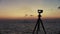 Photo camera on the beach at sunset on the Sea. Oil refinery factory in silhouette and sunset sky. Thailand.