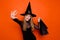 Photo of carefree friendly girl dressed dark witch dress headwear waving arm palm rising bargains isolated orange color