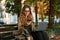 Photo of caucasian girl using mobile phone and laptop while sitting on bench in sunlit alley