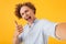 Photo of caucasian joyous man 20s taking selfie photo and showing thumb up, isolated over yellow background