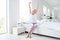 Photo of charming aged lady barefoot legs woman stretching eyes closed raise hands wear pajama white linen bed room