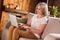 Photo of charming cute retired woman dressed white t-shirt sitting couch typing modern device smiling indoors flat home