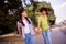 Photo of charming sweet friends couple dressed backpacks earphones holding arms walking smiling outdoors outside city