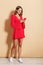 Photo of charming woman wearing red dress smiling and holding cellphone