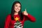 Photo of cheerful funky girl dressed ugly print red x-mas pullover showing thumb up isolated green color background