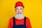 Photo of cheerful funny senior guy dressed uniform overall red hardhat smiling isolated yellow color background
