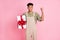 Photo of cheerful guy hold surprise box raise fist look camera wear beige overall isolated pink color background