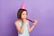 Photo of cheerful happy festive small girl hold hands noisemaker wear cone hat isolated on purple color background