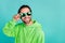 Photo of cheerful interested funny guy look empty space wear sunglass green hoodie isolated teal color background