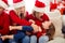 Photo of cheerful mommy mom girl kid sit couch tickle younger sister wear santa claus cap in house with x-mas decoration