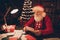 Photo of cheerful nice santa claus sit table dark evening read letter wear hat sweater in north pole office indoors