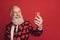 Photo of cheerful old man hold telephone make selfie beaming smile wear heart print suit tie  red background