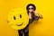 Photo of cheerful positive happy lady point finger smile hold hand emoji paper pinata isolated on yellow color