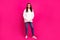 Photo of cheerful positive pretty lady hands pockets wear white hoodie jeans shoes isolated pink color background