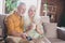 Photo of cheerful pretty pensioner lady gentleman sitting couch hugging drinking tea watching tv smiling indoors house