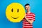 Photo of cheerful young happy man hold big face pinata smile emoji isolated on blue color background