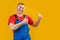 Photo of cheery optimistic young worker man or builder in blue uniform isolated over yellow background and shows thumbs up. Copy