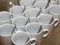 Photo closely standing diagonal rows together 13 white porcelain mugs with stainless steel spoons